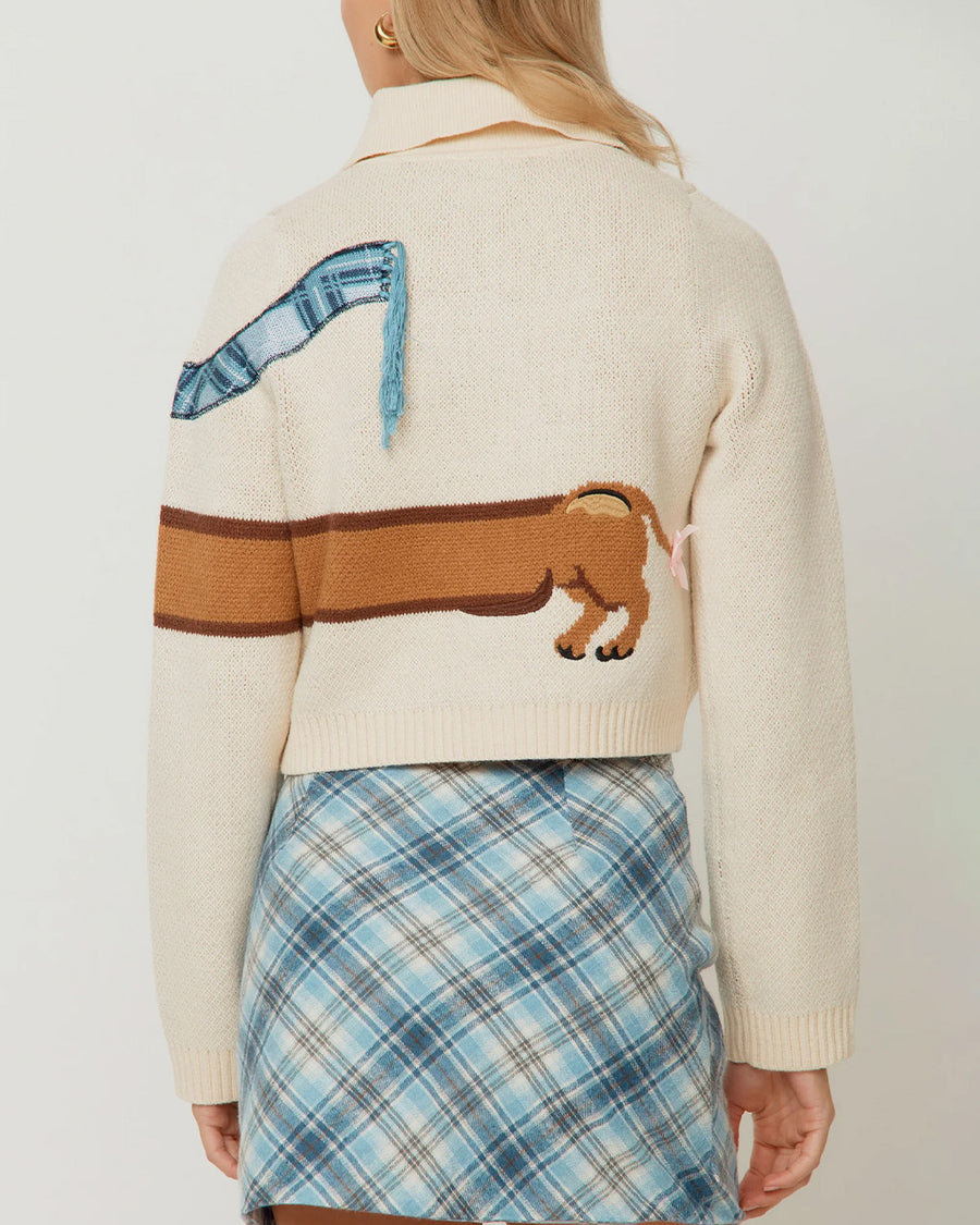 back view of model wearing cream cropped cardigan with a dog wearing a blue plaid scarf across the front and back