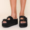 model wearing black suede platform slide sandals with oversized buckles and grommets