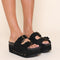 model wearing black suede platform slide sandals with oversized buckles and grommets