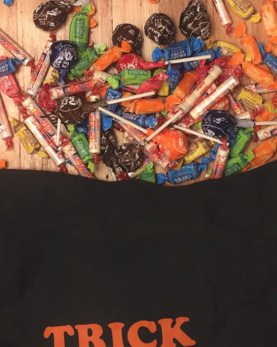 reverse side of black pillowcase style trick or treat bag that has all the peanut characters in costume and says 'TRICK OR TREAT' with candy spilling out