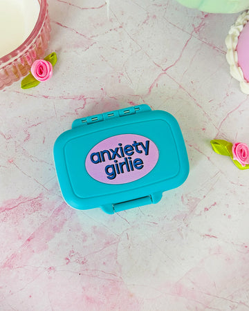 blue pill case with pink circle with 'anxiety girlie' across the front