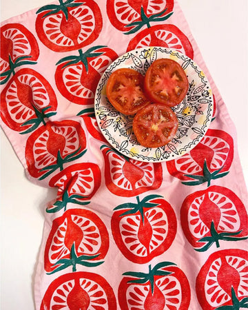 pink tea towel with stamped tomato print and plate of sliced tomatoes on it