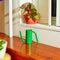 small green watering can with elongated spout and handle on wooden ledge