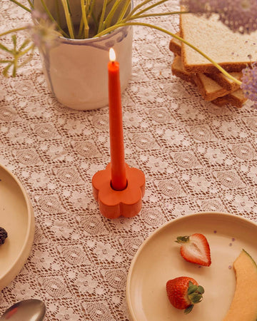 red flower shaped holder with a taper candle in it on table setting
