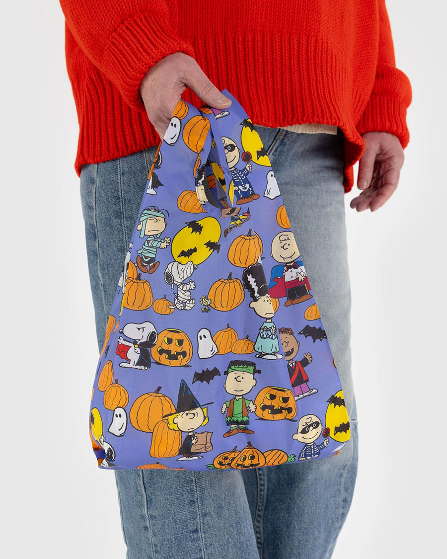 model holding blue baby baggu with the peanuts characters dress in various halloween costumes and surrounded by pumpkins/jack o'lanterns