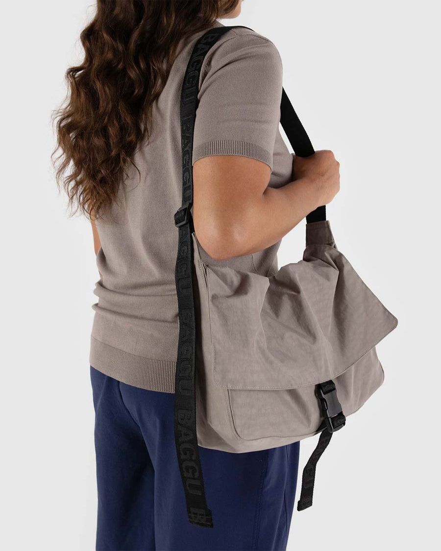 model carrying taupe large messenger bag with black strap and closure 