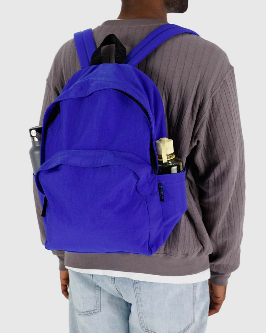 model wearing large bright blue nylon backpack with two front zipper compartments and drink holder on the side