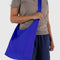 model carrying large bright blue nylon sling bag with adjustable strap