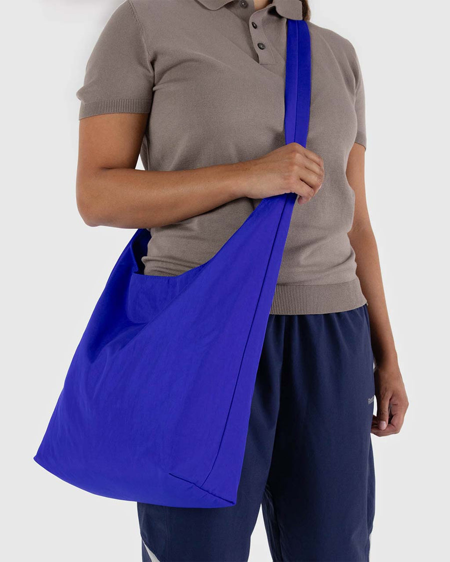 model carrying large bright blue nylon sling bag with adjustable strap