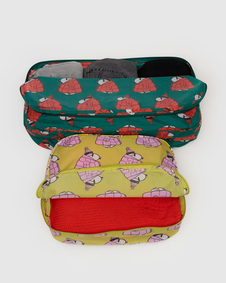 set of two large packing cubes: yellow with snoopy wearing pink puffer coat, and green with snoopy wearing a red puffer coat with items inside