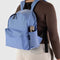 model wearing cornflower medium nylon backpack with large zipper compartment, front zipper pocket, and side drink holder