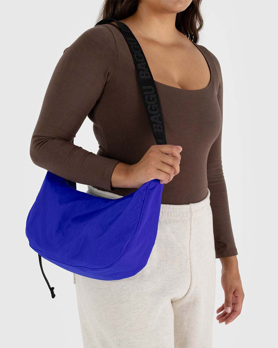 model carrying bright blue medium nylon crescent bag with black strap