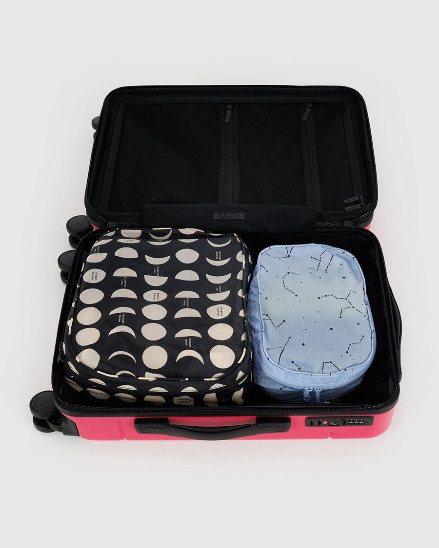 set of 2 packing cubes: light blue constellation, and black with cream moon phases in a suitcase