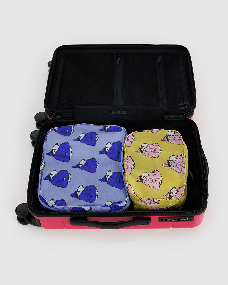 set of 2 packing cubes with yellow with snoopy in a pink puffer coat and blue with snoopy wearing a blue puffer coat in a suitcase