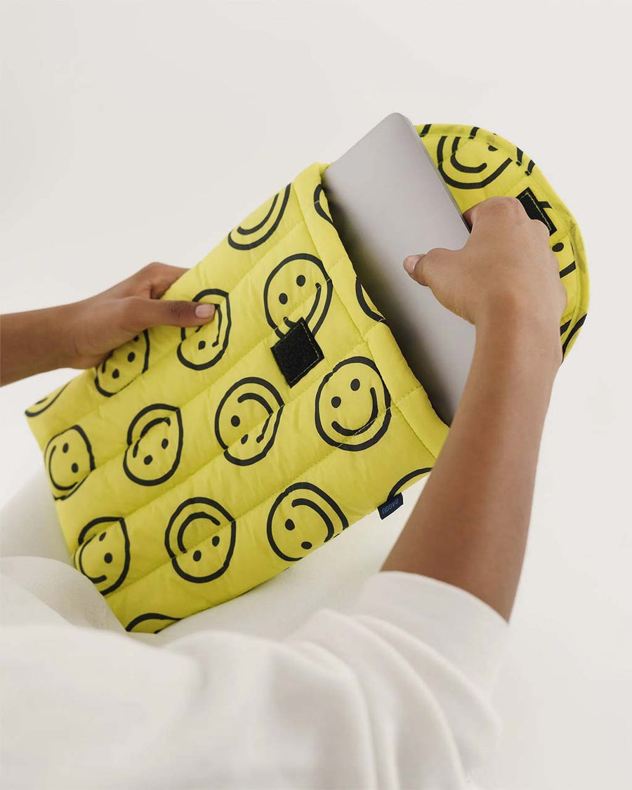 model pulling laptop of out yellow 13" puffy laptop sleeve with black all over smiley face print