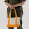 model holding tan small boat tote with tangerine accents