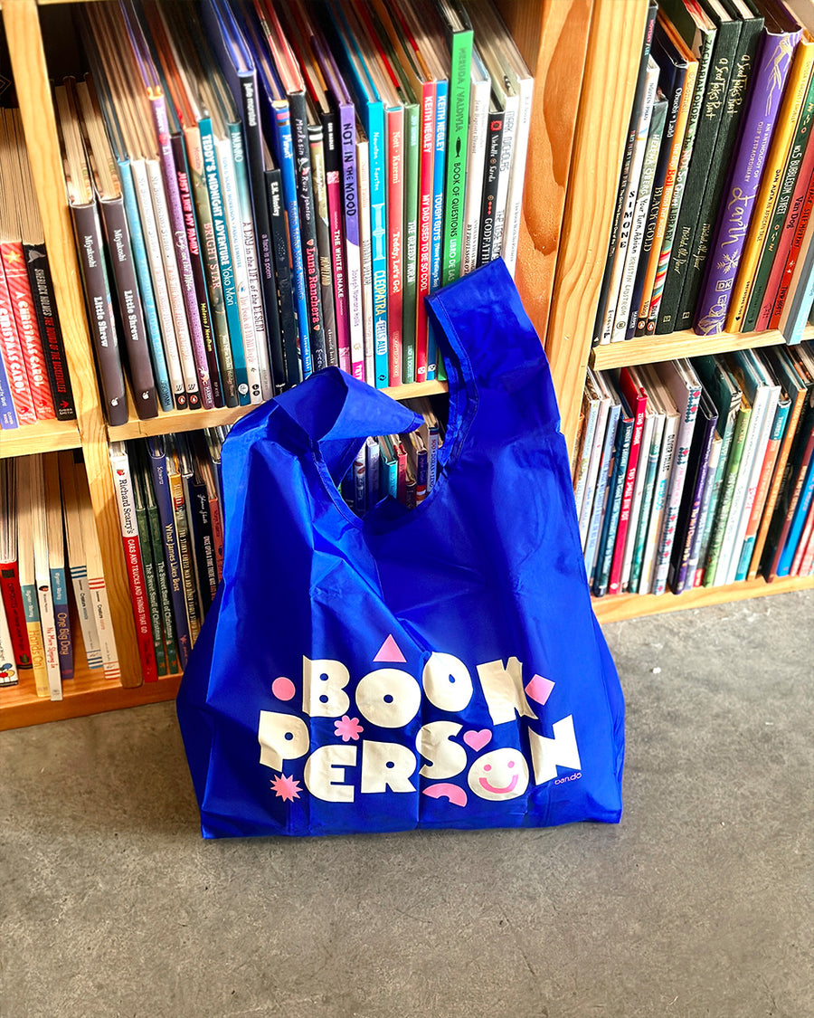 royal blue standard baggu with white 'book person' and pink shapes across the front in a library