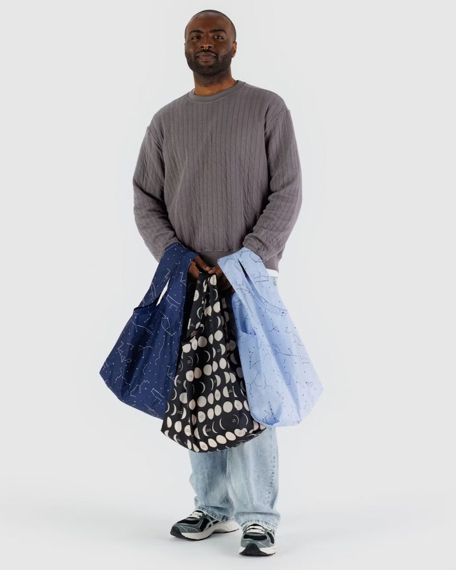 model carrying set of three standard baggu bags: black moon, light blue constellation and dark navy constellation