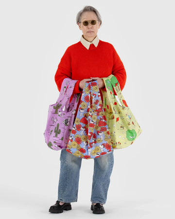 model holding standard baggus with pink spike bag, periwinkle joe cool and floral print and yellow charlie brown and friends flying a kite