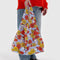 model holding periwinkle standard baggu with all over red and yellow floral and joe cool print