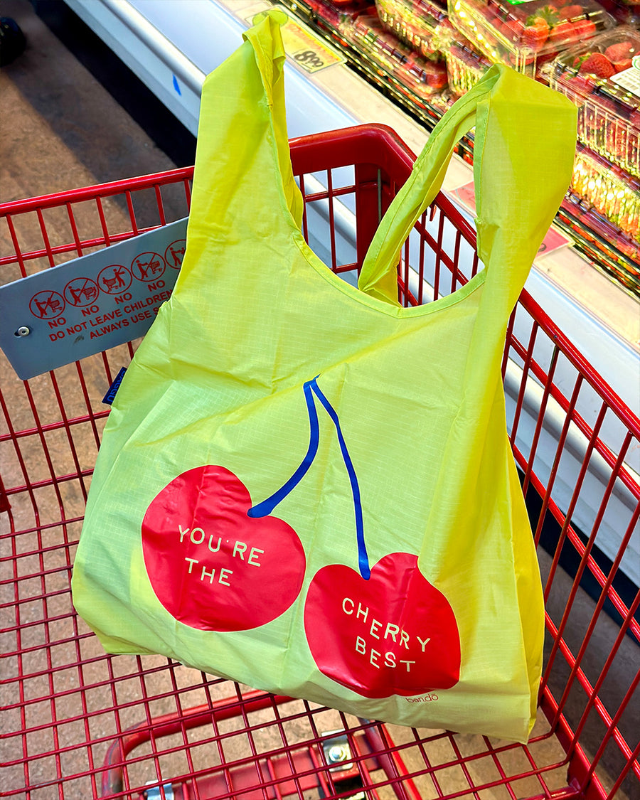 yellow standard baggu with red cherries and 'you're the cherry best' across the front in a grocery cart