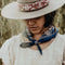 model wearing blue square bandana with pink mountain scene and floral print around their neck