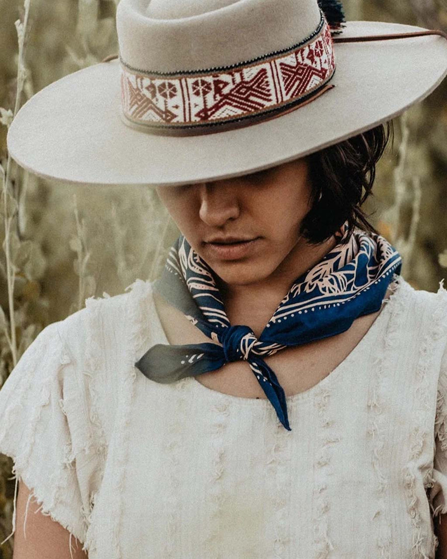 model wearing blue square bandana with pink mountain scene and floral print around their neck