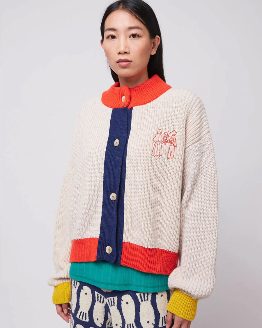 model wearing cream knit cardigan with yellow sleeve cuffs, coral trim and navy button front with embroidered couple on bust