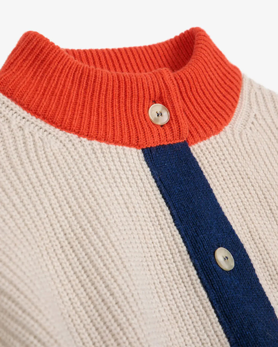 up close of cream knit cardigan with yellow sleeve cuffs, coral trim and navy button front with embroidered couple on bust
