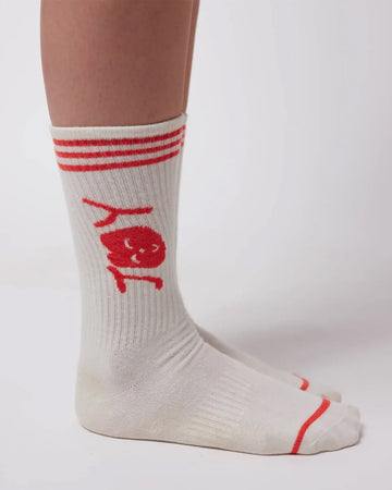 model wearing white crew socks with red trim and red 'joy' on the cuff
