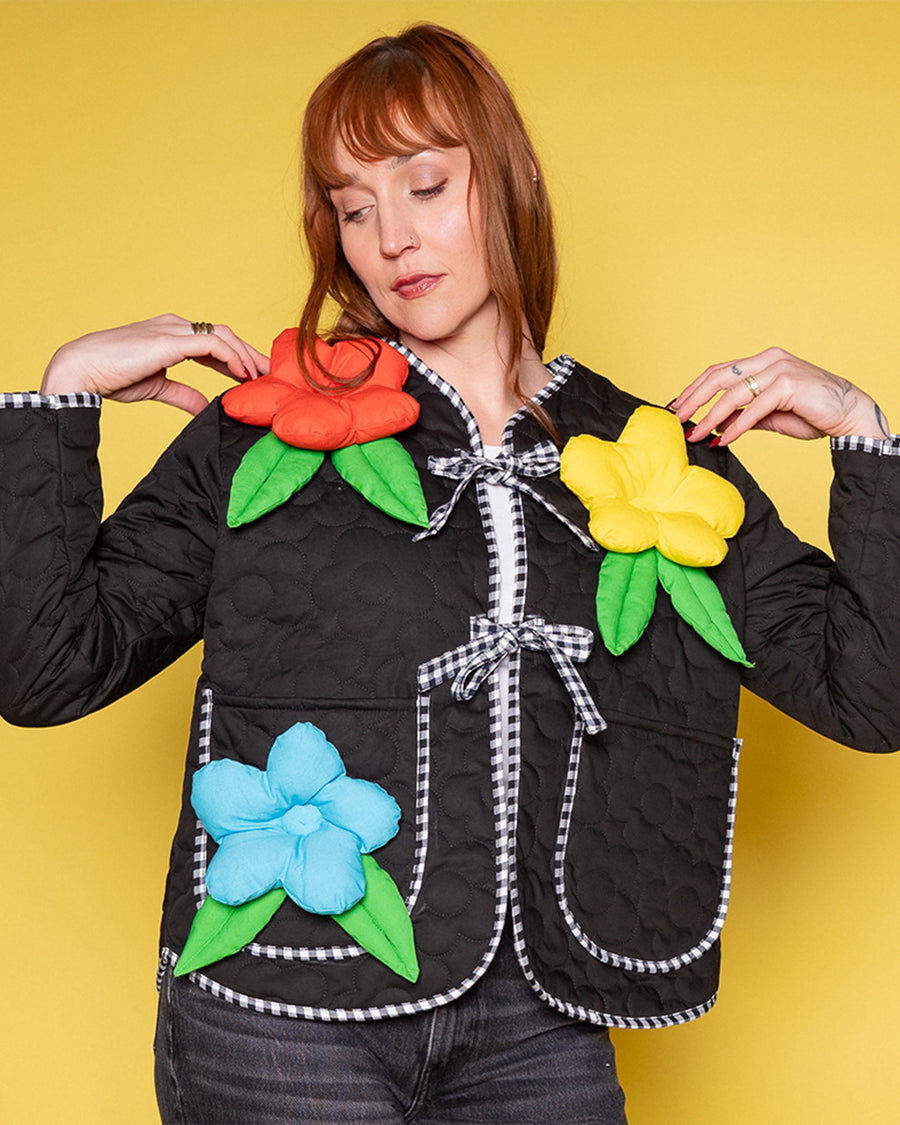 model wearing model wearing black quilted jacket with black and white stripe trim, and 3D red, yellow and blue flower print