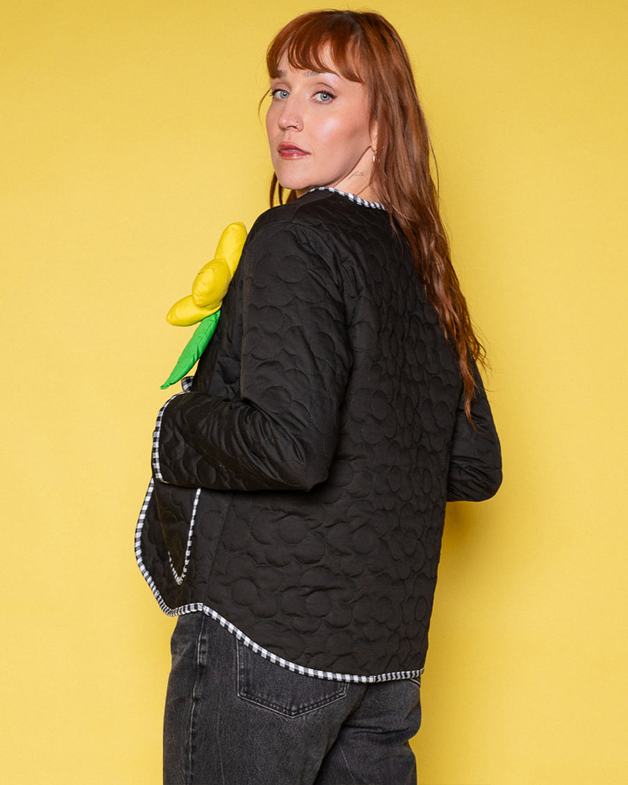 back view of model wearing black quilted jacket with black and white stripe trim, and 3D red, yellow and blue flower print