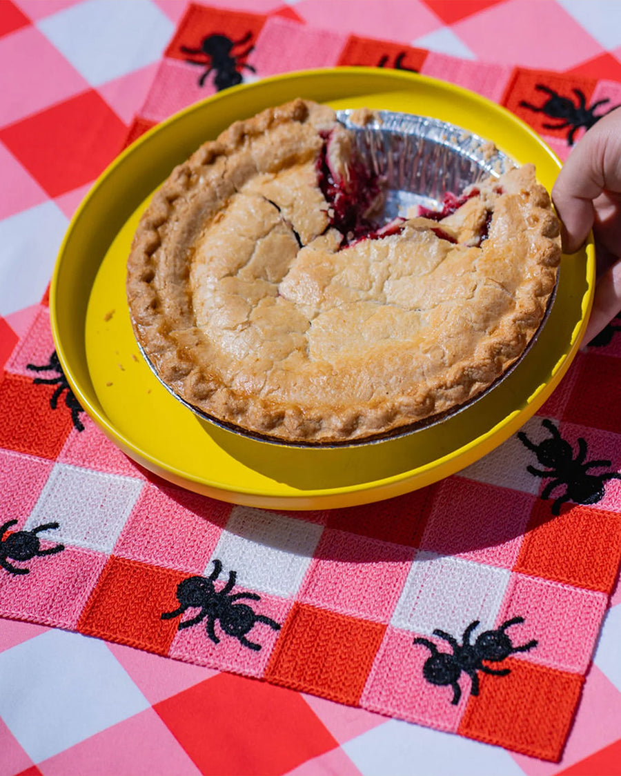 pink and white plaid placemat with black ant border with a pie on it