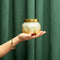 model holding gold and white glimmer candle with gold lid