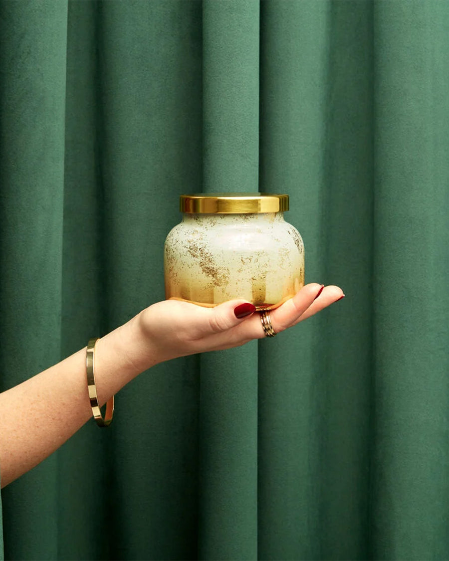 model holding gold and white glimmer candle with gold lid