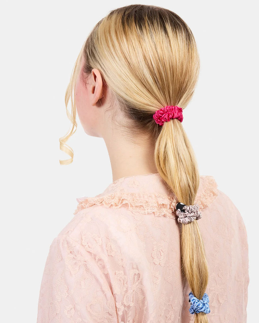 model wearing set of three skinny silk hair scrunchies: grey, hot pink and periwinkle in their hair