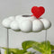 white cloud shaped houseplant waterer with red heart charm in a potted plant