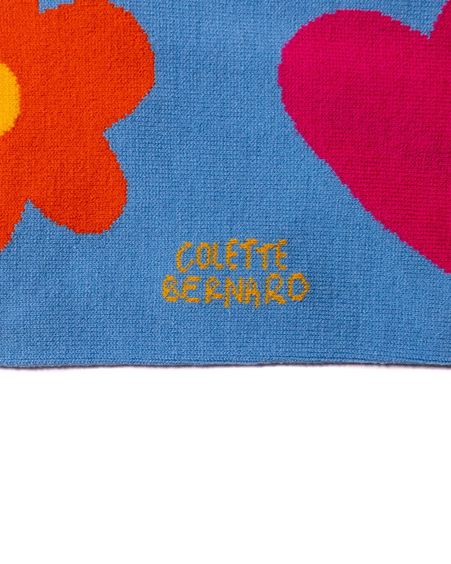 up close of blue rectangle scarf with colorful tassels on the end and yellow diamond, orange flower and pink heart design