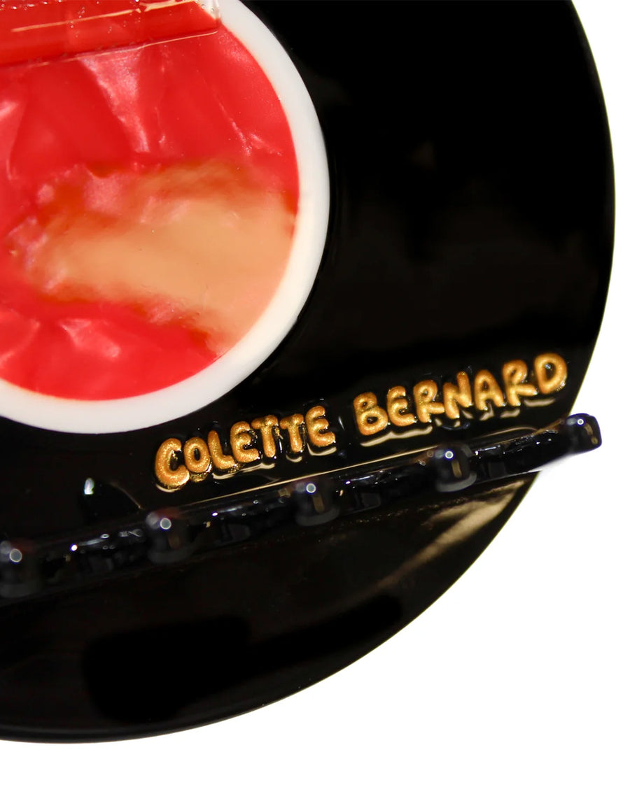 up close of colette bernard stamping on vinyl record hair claw with red center