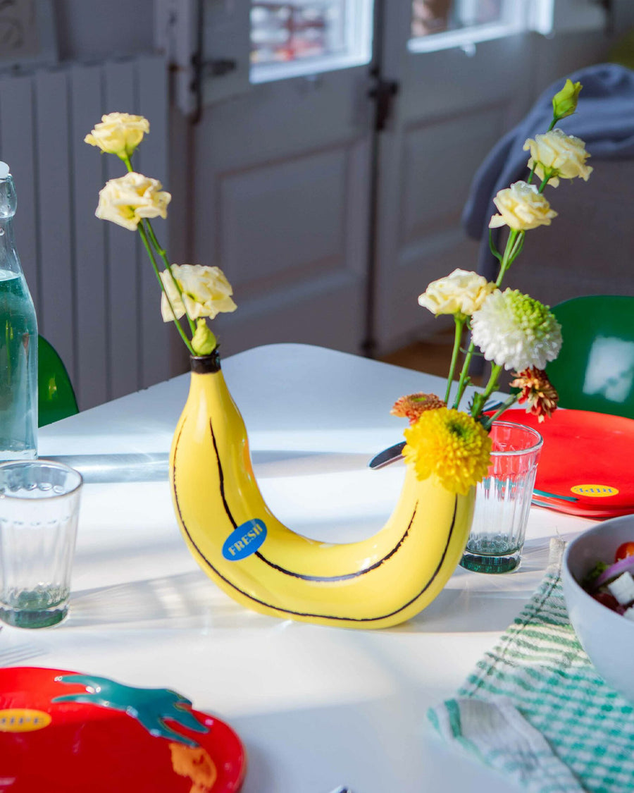 banana shaped vase with flowers on each side on a table