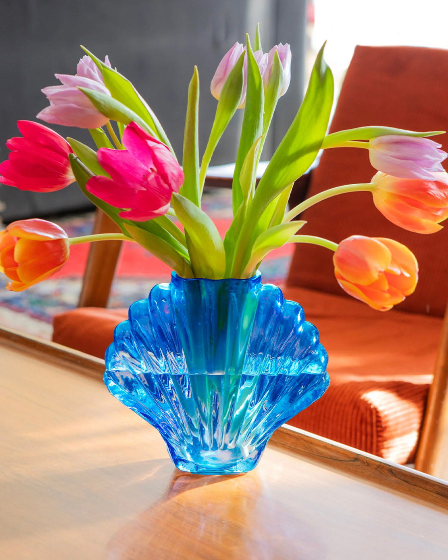cobalt blue glass seashell vase with tulips inside on a table