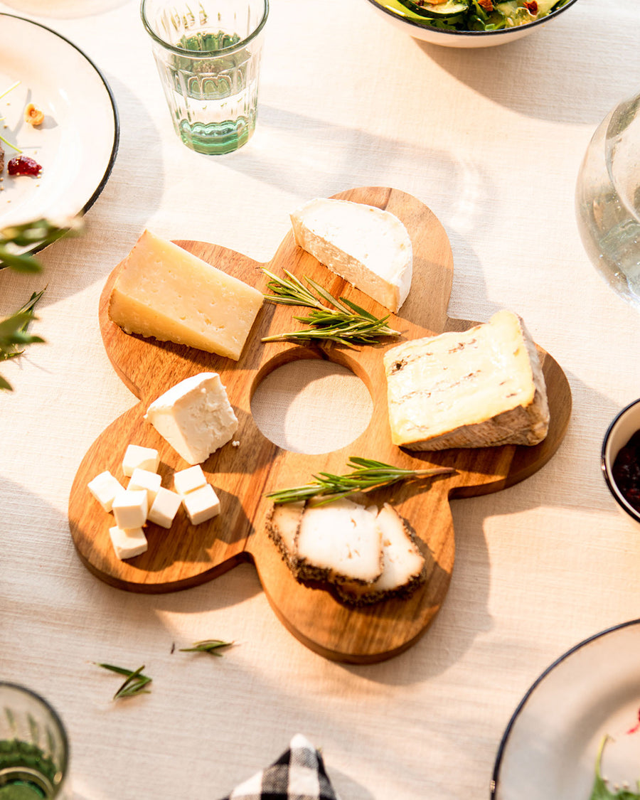 wooden daisy shaped serving board with various cheeses on it