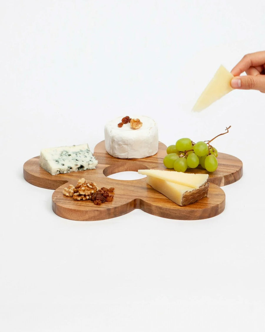 model taking cheese from wooden daisy shaped serving board with various cheeses on it