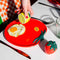 model putting pepper on her egg on a tomato shaped plate with yellow 'ripe' sticker on the left side