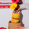 model pulling cheeseburger shaped vase with flowers from a brown paper bag