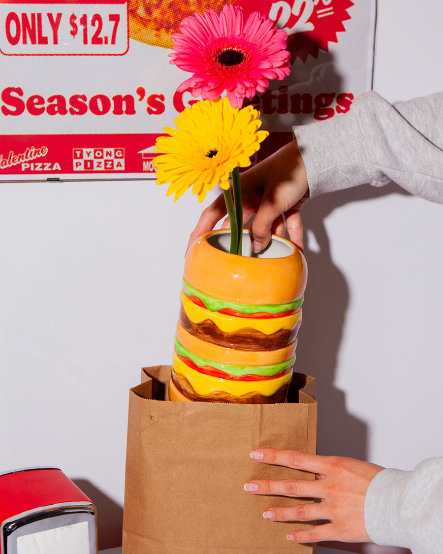 model pulling cheeseburger shaped vase with flowers from a brown paper bag