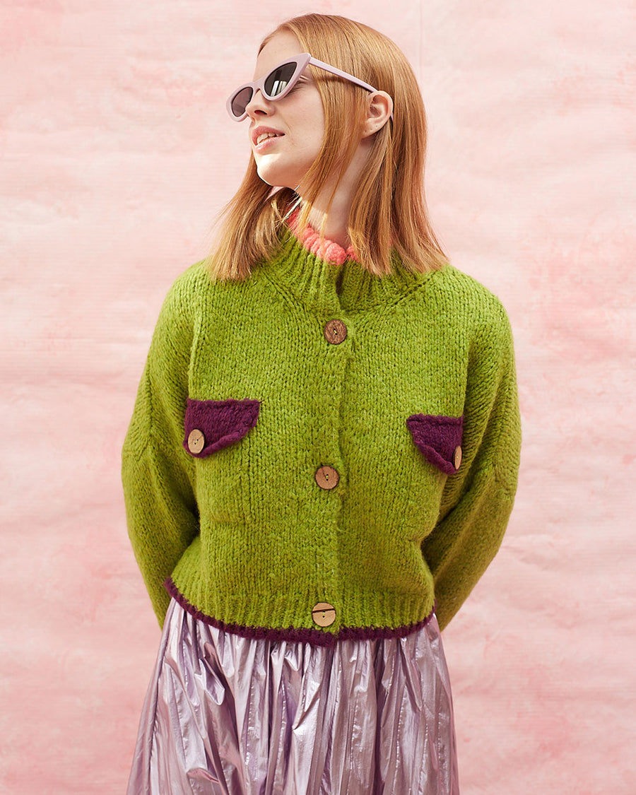 model wearing slightly cropped pea green cardigan with plum patch pockets and trim