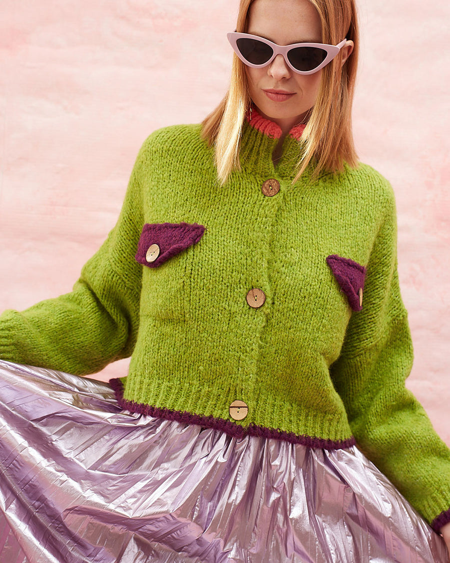 model wearing slightly cropped pea green cardigan with plum patch pockets and trim