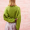 back view of model wearing slightly cropped pea green cardigan with plum patch pockets and trim