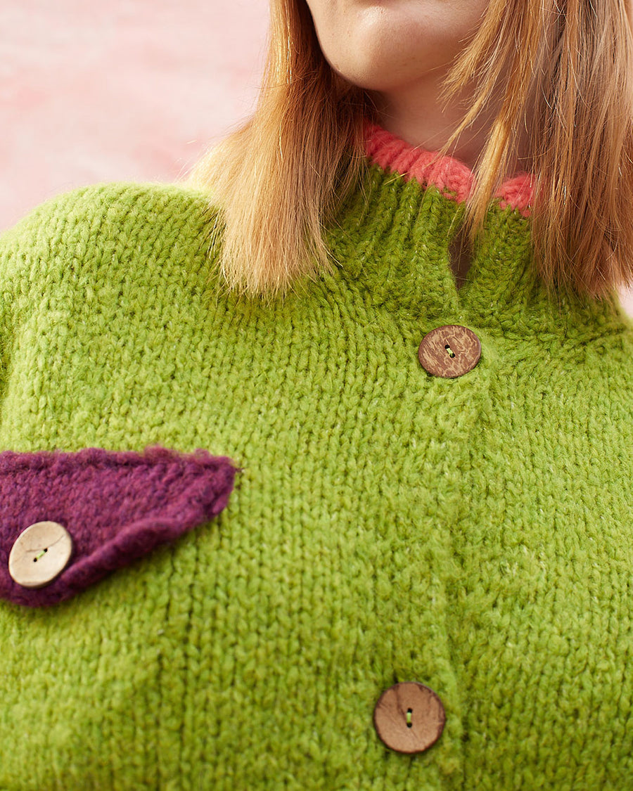 up close of model wearing slightly cropped pea green cardigan with plum patch pockets and trim